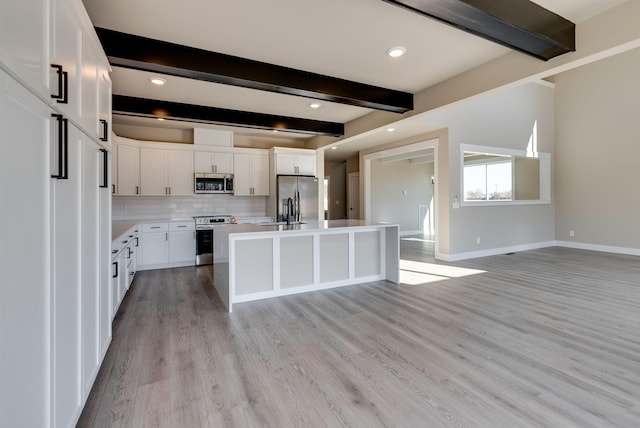 kitchen with a kitchen island, appliances with stainless steel finishes, white cabinets, and beam ceiling