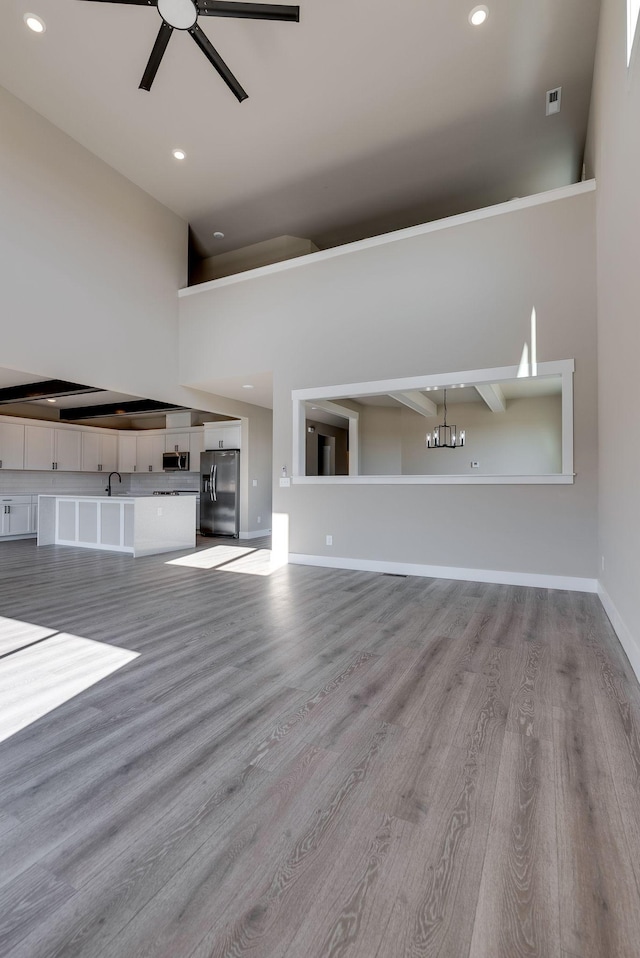 unfurnished living room featuring sink, light hardwood / wood-style floors, ceiling fan, and a high ceiling