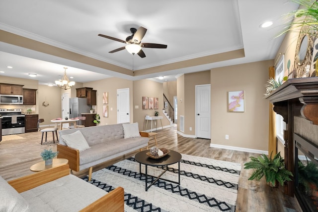 living room with crown molding, ceiling fan with notable chandelier, light hardwood / wood-style flooring, and a tray ceiling