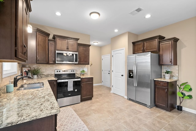 kitchen featuring stainless steel appliances, light stone countertops, sink, and dark brown cabinetry