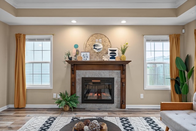 living room with ornamental molding, a tiled fireplace, wood-type flooring, and a wealth of natural light