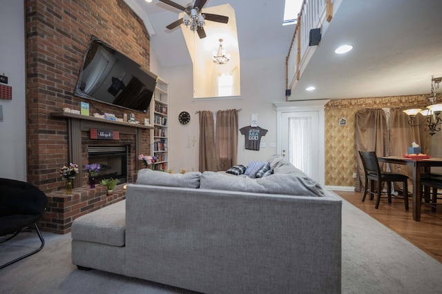 living room with ceiling fan with notable chandelier, a towering ceiling, hardwood / wood-style floors, and a fireplace