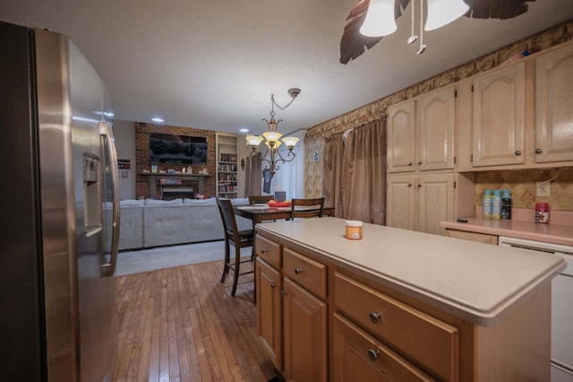 kitchen featuring hardwood / wood-style flooring, stainless steel fridge, ceiling fan, a center island, and a brick fireplace