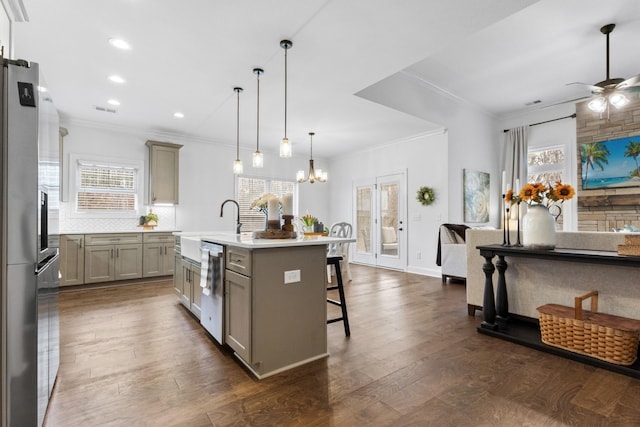 kitchen featuring gray cabinets, a breakfast bar, appliances with stainless steel finishes, a kitchen island with sink, and decorative light fixtures