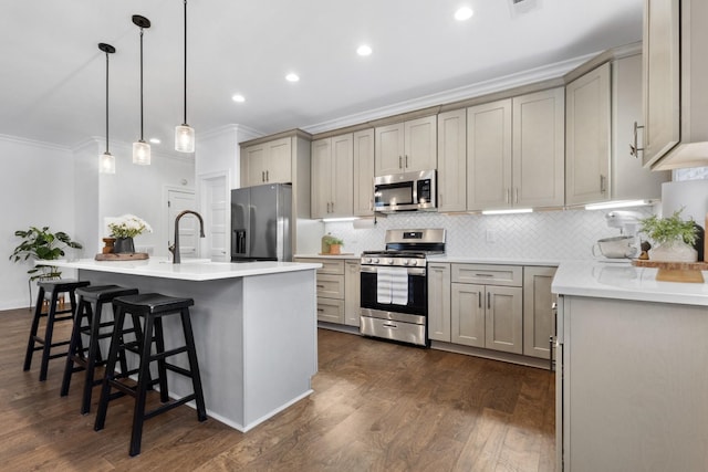 kitchen with a breakfast bar, hanging light fixtures, ornamental molding, an island with sink, and stainless steel appliances