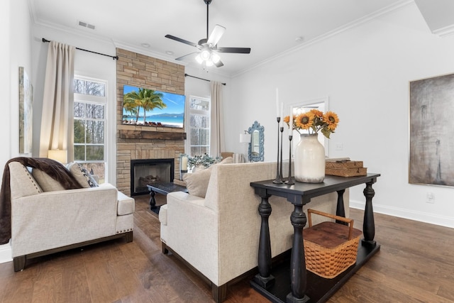 living room with dark wood-type flooring, ceiling fan, ornamental molding, and a stone fireplace