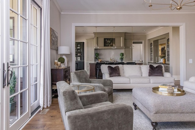 living room featuring an inviting chandelier, wood-type flooring, and ornamental molding