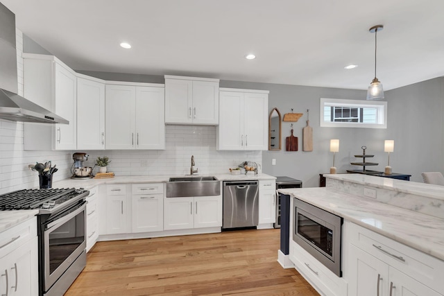 kitchen featuring a sink, white cabinetry, appliances with stainless steel finishes, light stone countertops, and wall chimney exhaust hood