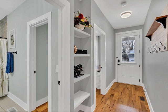 doorway with light wood-type flooring, visible vents, and baseboards