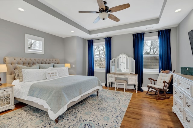 bedroom featuring baseboards, visible vents, wood finished floors, a tray ceiling, and recessed lighting