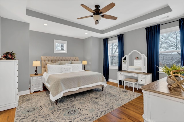 bedroom featuring wood finished floors, multiple windows, a raised ceiling, and visible vents