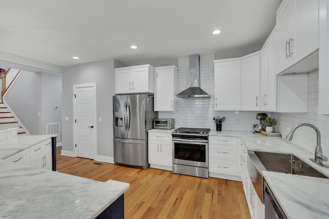 kitchen with stainless steel appliances, wall chimney range hood, light wood finished floors, and tasteful backsplash