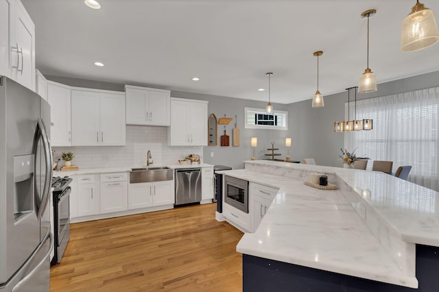 kitchen with appliances with stainless steel finishes, white cabinetry, a sink, and light wood finished floors