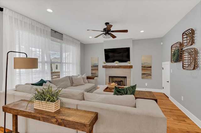 living area with light wood-style floors, baseboards, a tiled fireplace, and recessed lighting