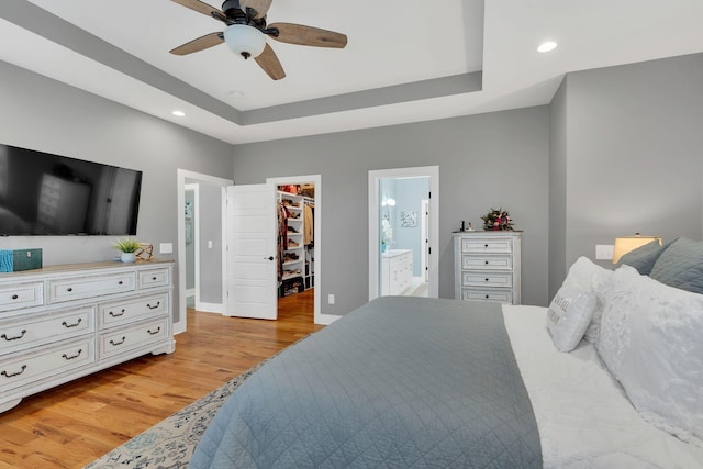 bedroom with a spacious closet, a tray ceiling, recessed lighting, and light wood-style floors