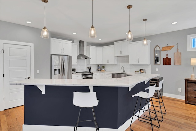 kitchen featuring light wood-style flooring, a sink, appliances with stainless steel finishes, backsplash, and wall chimney exhaust hood