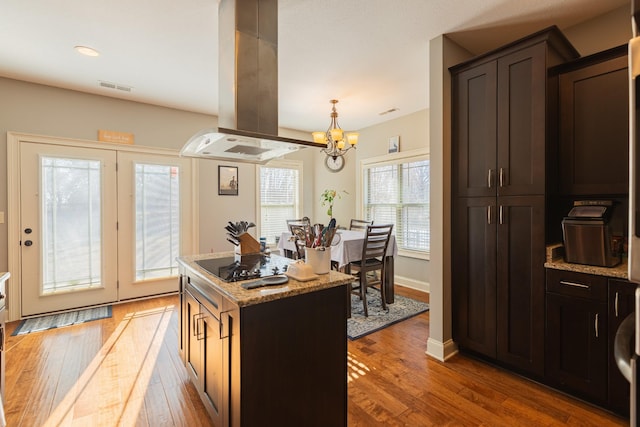 kitchen with hardwood / wood-style floors, a center island, light stone counters, island exhaust hood, and black electric cooktop