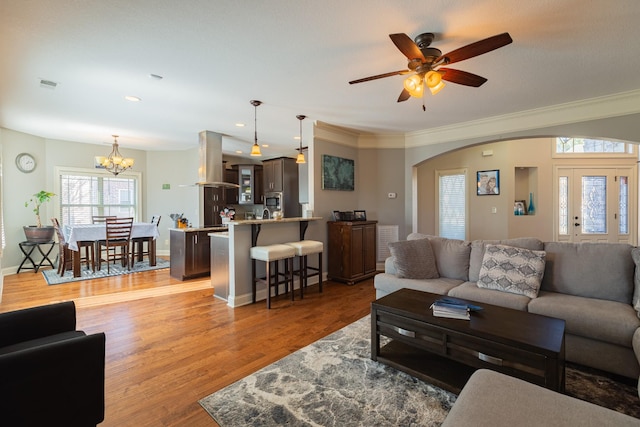 living room featuring ornamental molding, ceiling fan with notable chandelier, and light wood-type flooring