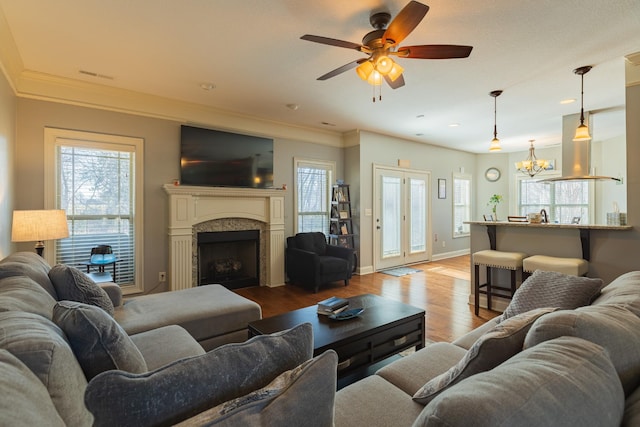 living room with crown molding, ceiling fan with notable chandelier, and light wood-type flooring