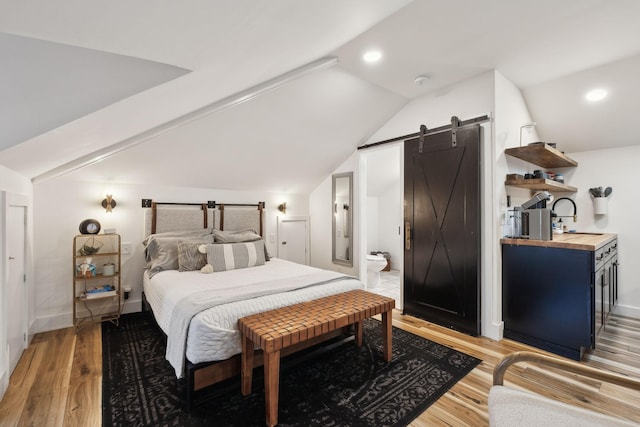 bedroom featuring vaulted ceiling, ensuite bathroom, sink, light hardwood / wood-style floors, and a barn door