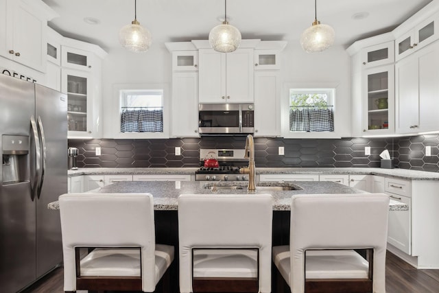 kitchen with hanging light fixtures, stainless steel appliances, white cabinets, and a center island with sink