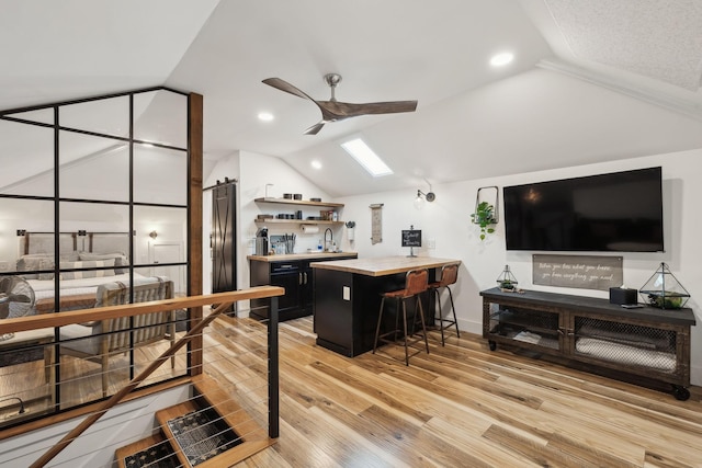 interior space with sink, light hardwood / wood-style flooring, ceiling fan, a kitchen breakfast bar, and vaulted ceiling with skylight