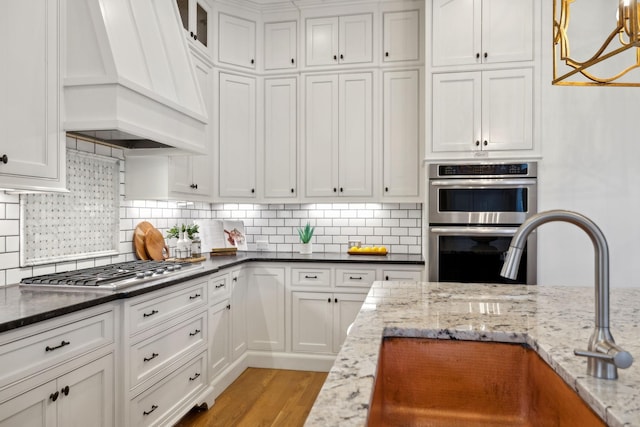 kitchen featuring dark stone countertops, appliances with stainless steel finishes, custom exhaust hood, and white cabinets