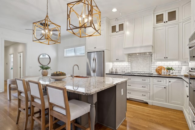 kitchen featuring sink, appliances with stainless steel finishes, a kitchen island with sink, white cabinetry, and decorative light fixtures