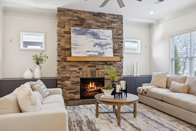 living room featuring ceiling fan, ornamental molding, and a stone fireplace