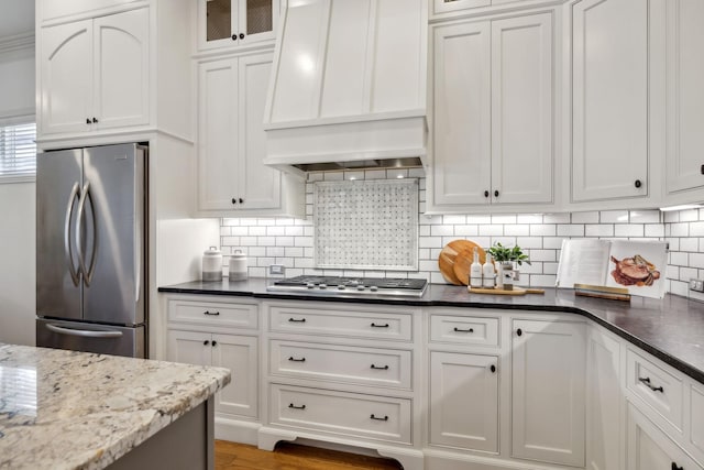 kitchen with backsplash, stainless steel appliances, custom range hood, white cabinets, and dark stone counters