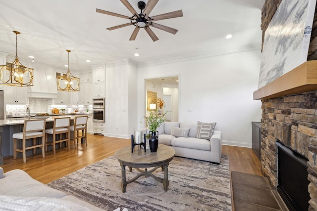 living room featuring sink, a fireplace, light hardwood / wood-style floors, ornamental molding, and ceiling fan with notable chandelier