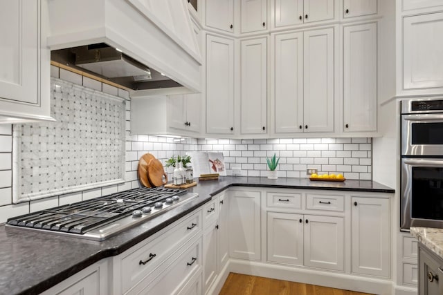 kitchen with backsplash, custom exhaust hood, white cabinets, and appliances with stainless steel finishes