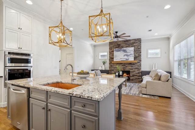 kitchen featuring a stone fireplace, sink, hanging light fixtures, stainless steel double oven, and a kitchen island with sink