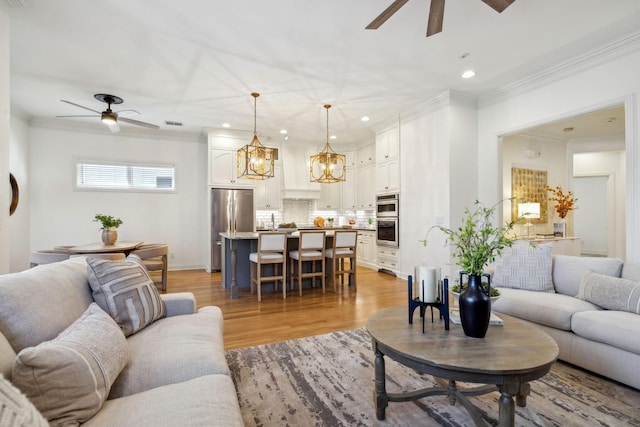 living room with crown molding, ceiling fan with notable chandelier, and light wood-type flooring