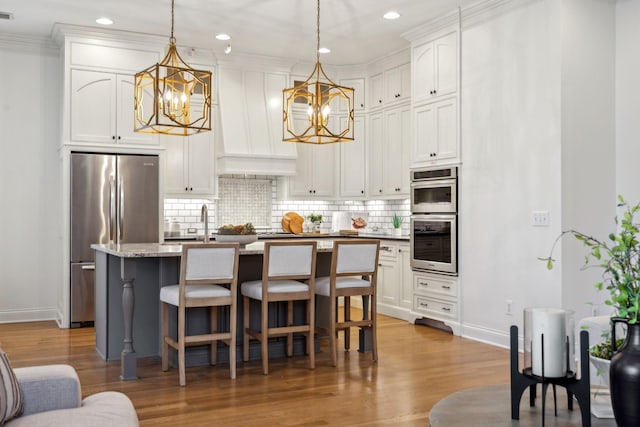 kitchen featuring white cabinetry, hardwood / wood-style flooring, pendant lighting, stainless steel appliances, and a kitchen island with sink