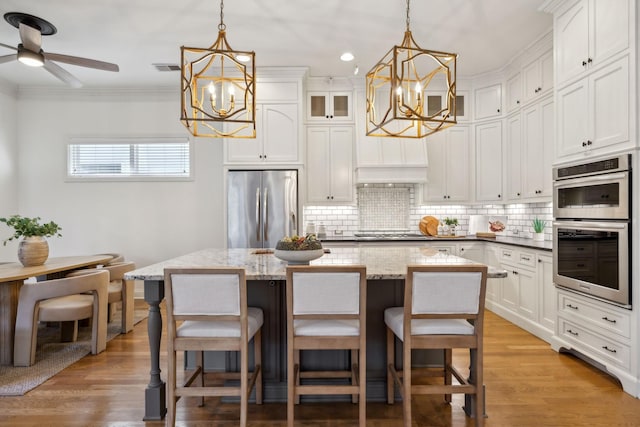 kitchen with white cabinetry, appliances with stainless steel finishes, a kitchen island, pendant lighting, and dark stone counters