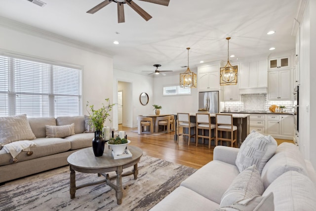 living room featuring ceiling fan, ornamental molding, and light hardwood / wood-style floors