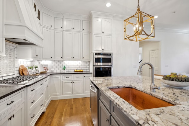 kitchen featuring appliances with stainless steel finishes, pendant lighting, white cabinetry, sink, and custom exhaust hood