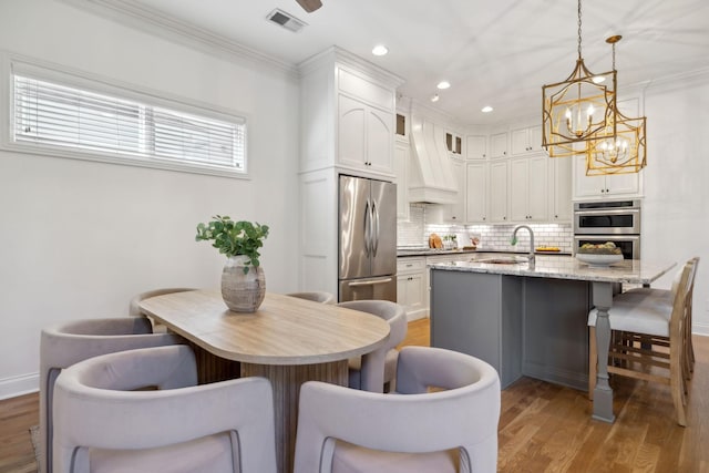 kitchen with decorative light fixtures, an island with sink, sink, white cabinets, and stainless steel appliances