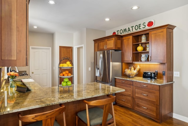 kitchen featuring a breakfast bar, light stone counters, built in desk, stainless steel fridge, and kitchen peninsula