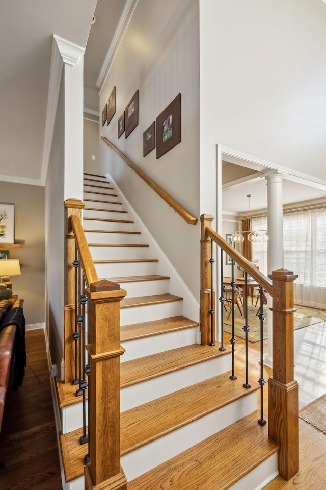 stairway with ornate columns, ornamental molding, hardwood / wood-style floors, and a chandelier