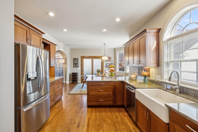 kitchen featuring sink, appliances with stainless steel finishes, decorative light fixtures, kitchen peninsula, and light wood-type flooring