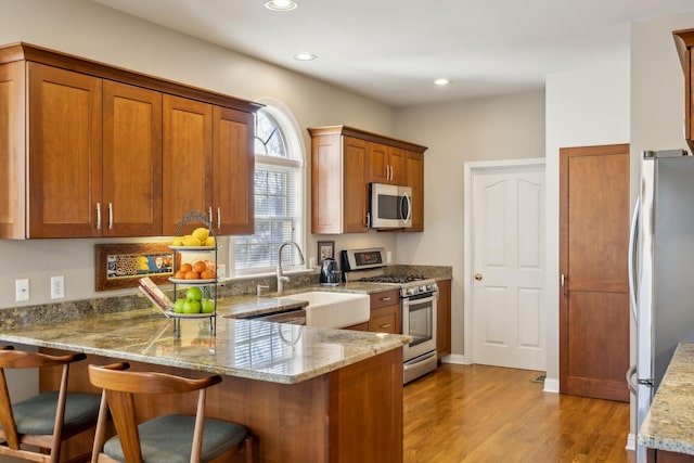 kitchen featuring stainless steel appliances, kitchen peninsula, sink, and light stone countertops