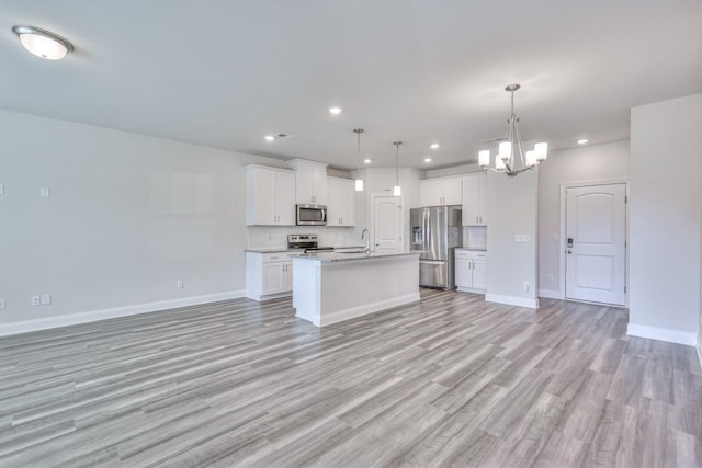 kitchen featuring pendant lighting, sink, white cabinets, stainless steel appliances, and a center island with sink