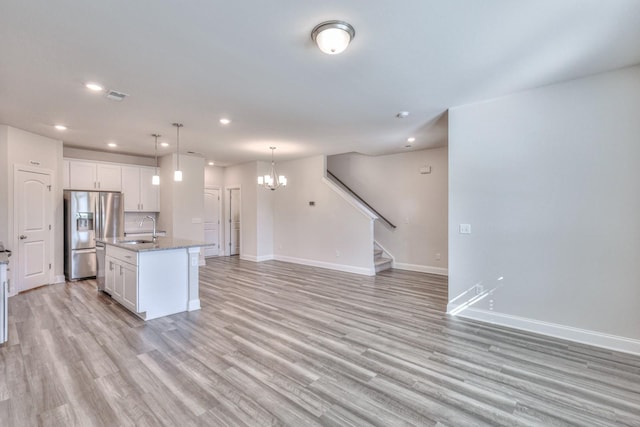 kitchen with sink, stainless steel fridge with ice dispenser, a center island with sink, and white cabinets