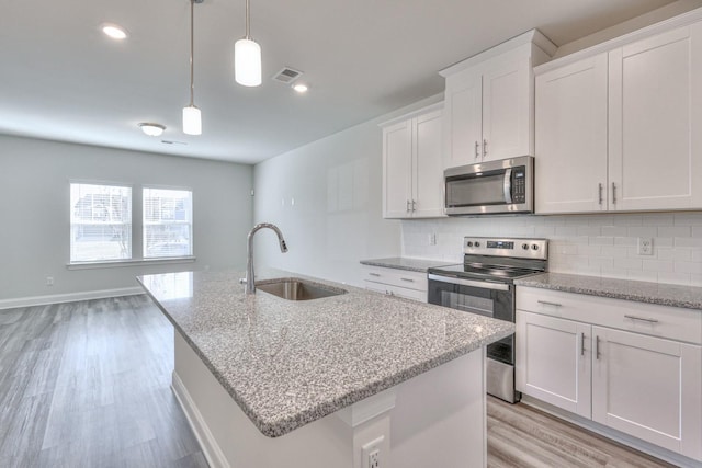 kitchen featuring sink, appliances with stainless steel finishes, pendant lighting, a kitchen island with sink, and white cabinets