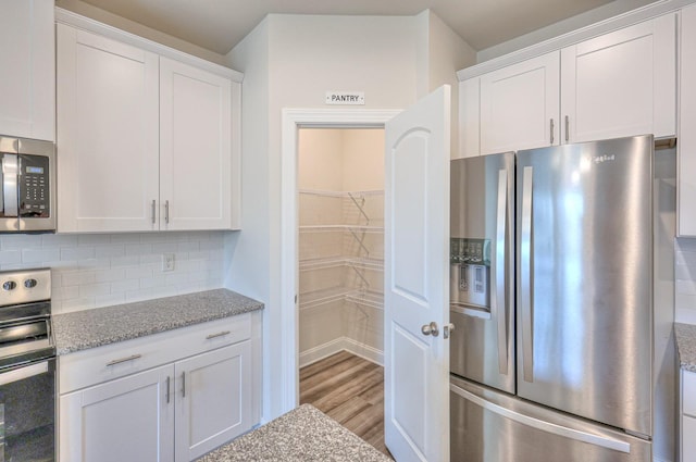 kitchen with white cabinetry, stainless steel appliances, light stone counters, tasteful backsplash, and light wood-type flooring