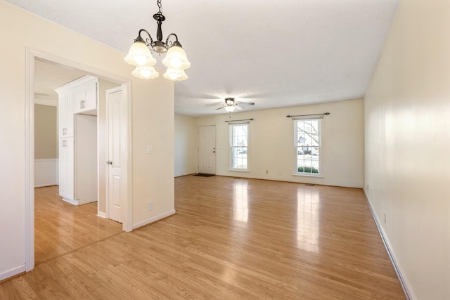 spare room featuring ceiling fan with notable chandelier, light hardwood / wood-style flooring, and a textured ceiling