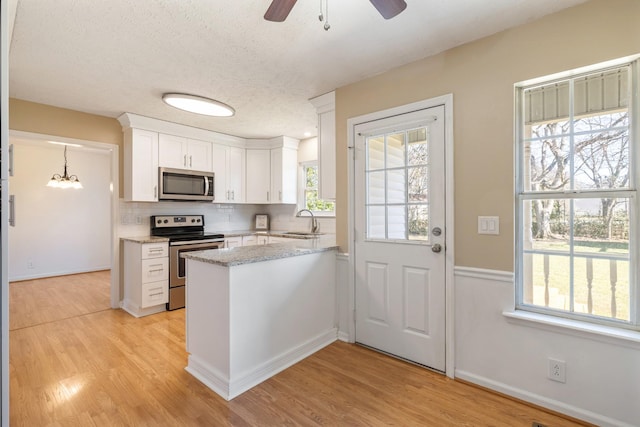 kitchen with pendant lighting, white cabinetry, stainless steel appliances, decorative backsplash, and light wood-type flooring