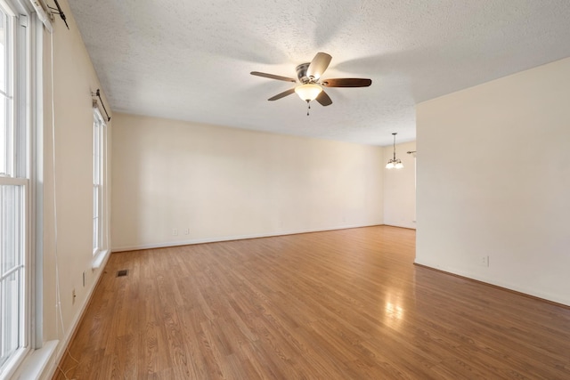 empty room with hardwood / wood-style flooring, ceiling fan with notable chandelier, and a textured ceiling